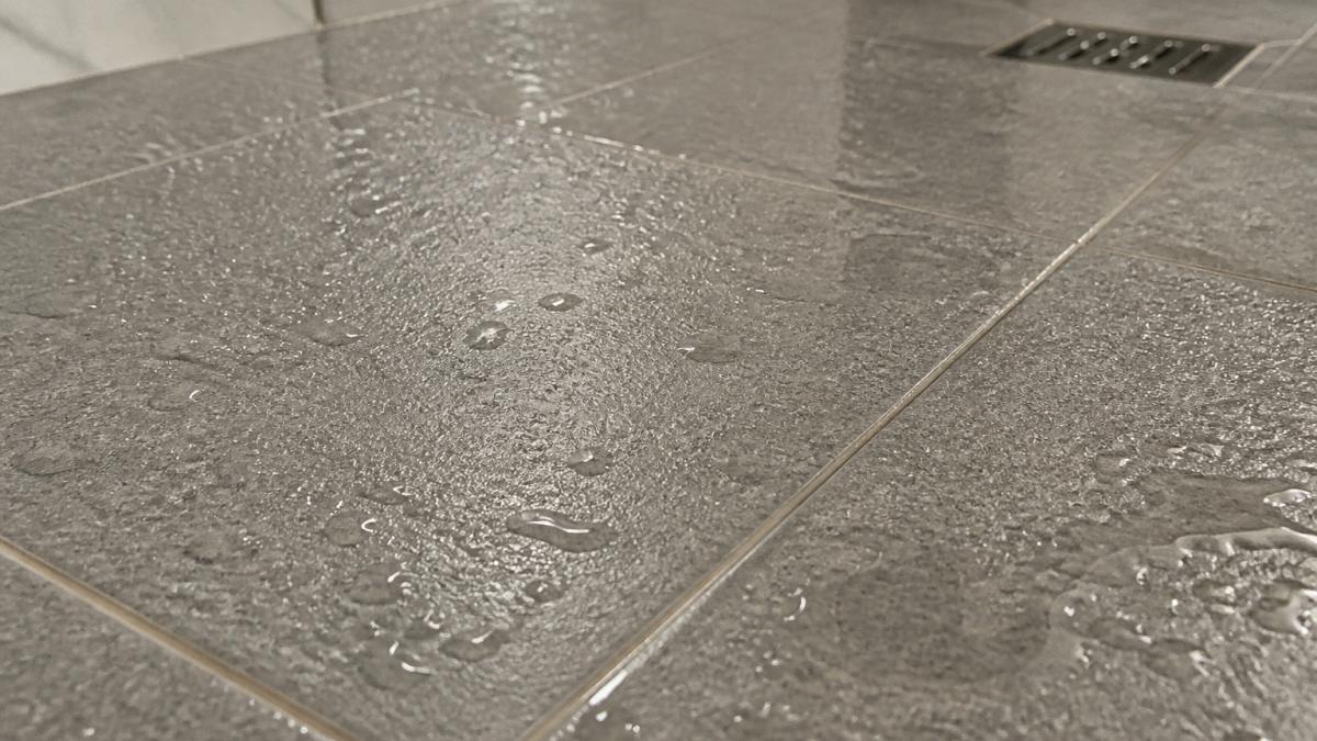 Close-up of wet bathroom floor tiles showing textured surface finish with water droplets visible on the grouted tile surface to illustrate slip resistance and traction on wet surfaces